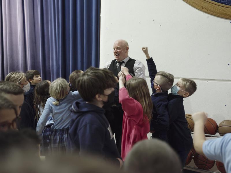 Student volunteer celebrating on stage during a Kansas City school assembly magic show